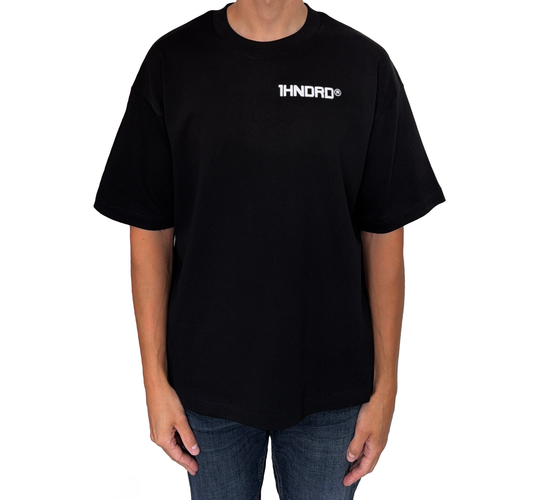 Man standing with arm by his side facing the camera wearing 1HNDRD® boxy fit T-shirt in Jet Black with bold puff print – British streetwear